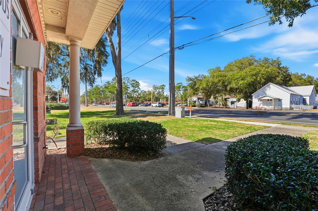 A brick-paved entryway with a pillar overlooks a grassy lawn, a road, and nearby buildings — 4130 NW 37TH PLACE Ste E, GAINESVILLE, FL