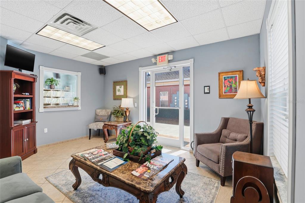 A waiting room features a coffee table, armchairs, a bookshelf, and a glass entry door — 4130 NW 37TH PLACE Ste E, GAINESVILLE, FL
