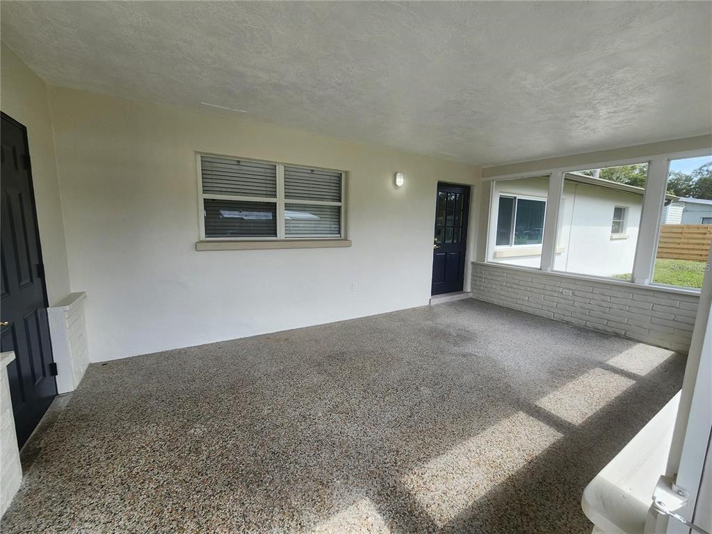 A covered patio with a textured concrete floor, white walls, and two dark doors — 109 21ST STREET NE, BRADENTON, FL