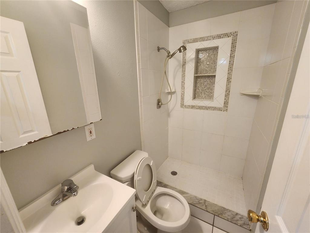 A small bathroom features a white vanity, a toilet, and a tiled walk-in shower — 109 21ST STREET NE, BRADENTON, FL