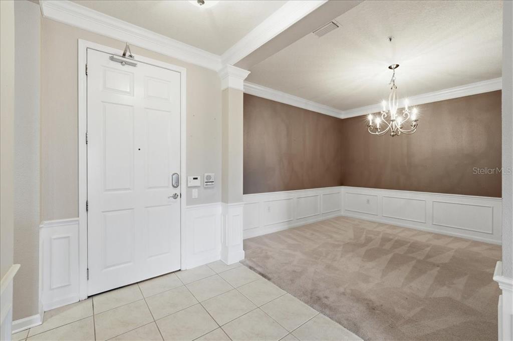 An entryway with tile flooring leads to a carpeted dining area featuring wainscoting and chandelier — 7903 SEMINOLE BOULEVARD UNIT 2305, SEMINOLE, FL