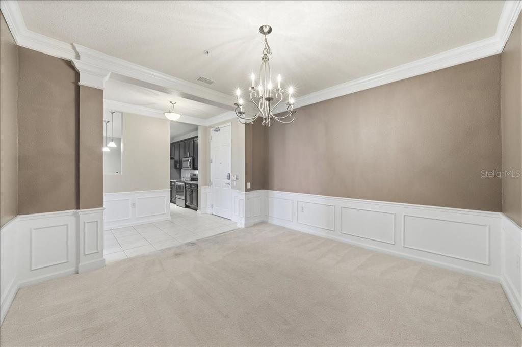 A dining room with beige walls, white wainscoting, carpeted flooring, and a central chandelier — 7903 SEMINOLE BOULEVARD UNIT 2305, SEMINOLE, FL
