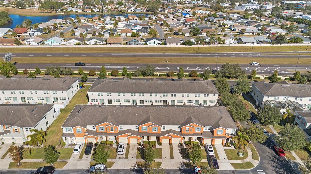 An aerial view shows a row of townhomes with driveways and a nearby highway — 5109 KILLARNEY WAY, KISSIMMEE, FL