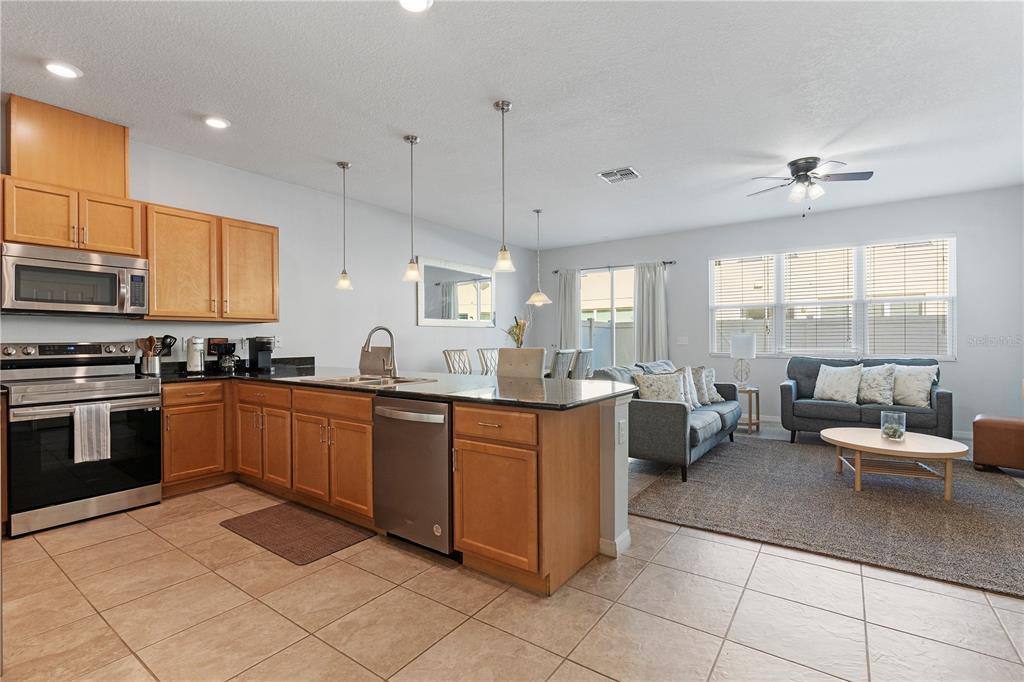 An open-concept kitchen with wood cabinets and a granite island overlooks a living room area — 5109 KILLARNEY WAY, KISSIMMEE, FL