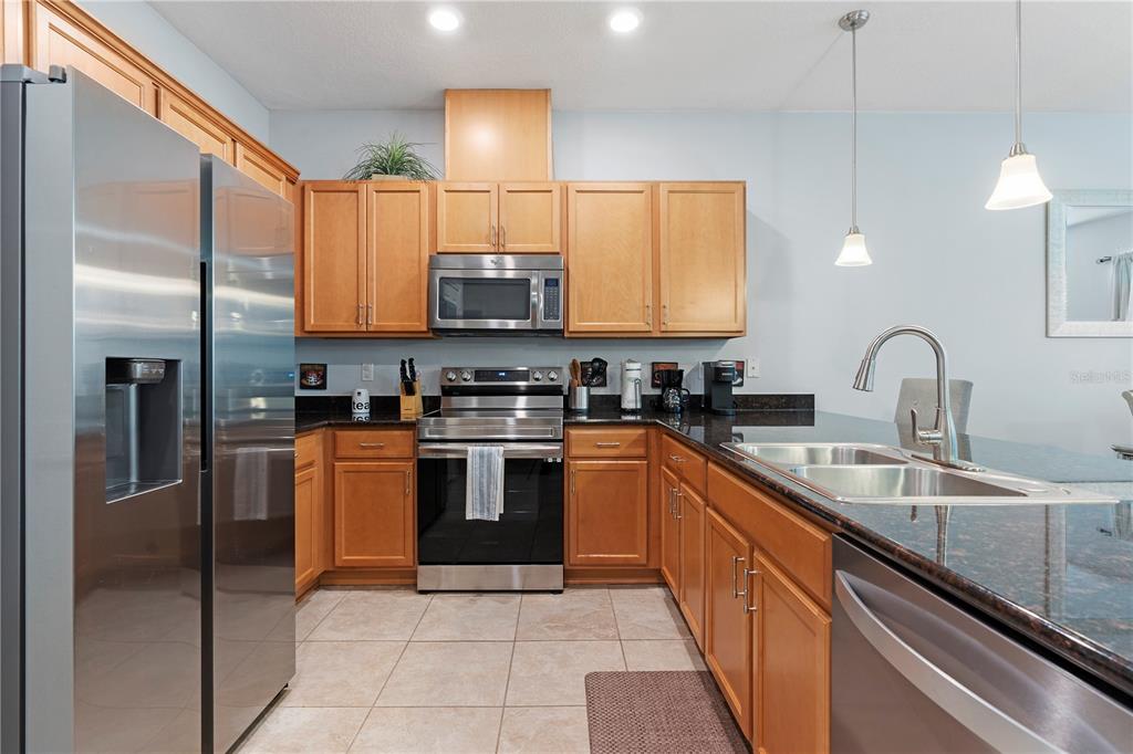 A kitchen features light wood cabinets, stainless steel appliances, and dark granite countertops — 5109 KILLARNEY WAY, KISSIMMEE, FL