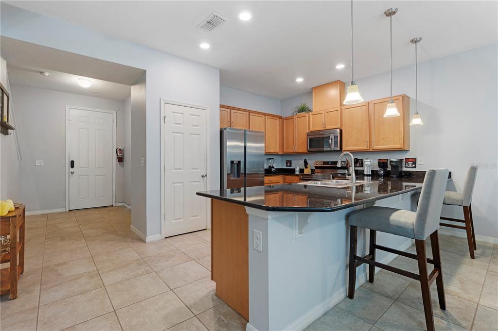 A kitchen features light wood cabinets, dark granite countertops, a center island, and two barstools — 5109 KILLARNEY WAY, KISSIMMEE, FL