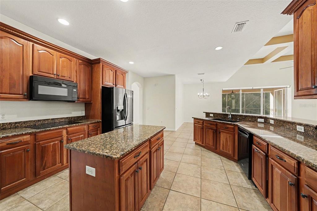 A kitchen with wood cabinets, granite countertops, a center island, and tile flooring — 14906 MAN O WAR DRIVE, ODESSA, FL