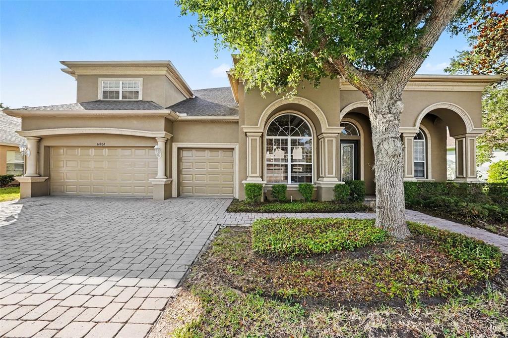 A single-story house with a paved driveway, two-car garage, arched windows, and a large tree — 14906 MAN O WAR DRIVE, ODESSA, FL