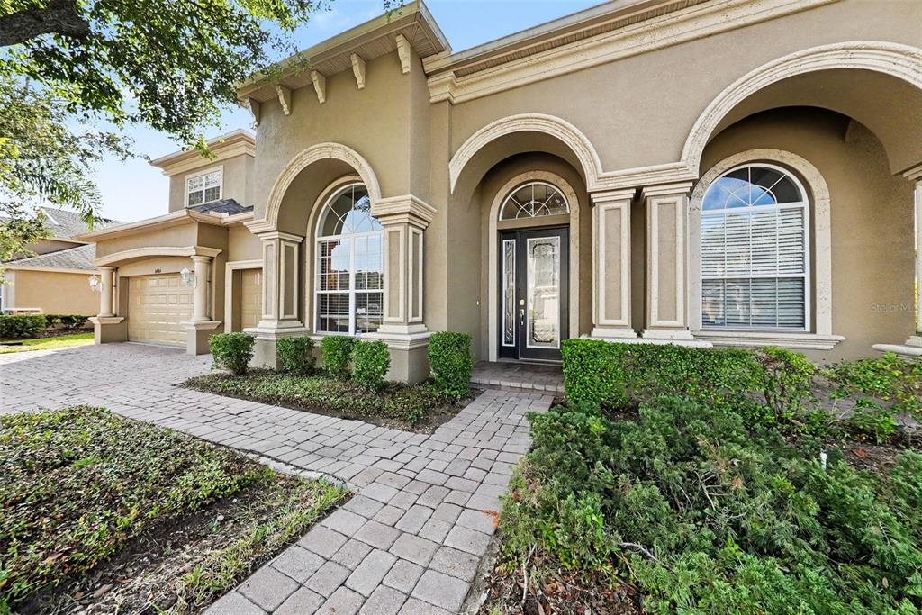 A tan stucco house features arched windows, decorative columns, and a paved walkway and driveway — 14906 MAN O WAR DRIVE, ODESSA, FL