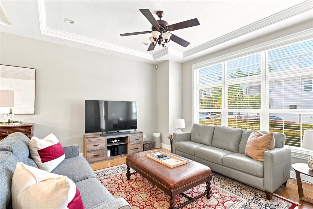 A living room features two sofas, a leather ottoman, a television, and large windows — 2557 W PLATT STREET, TAMPA, FL