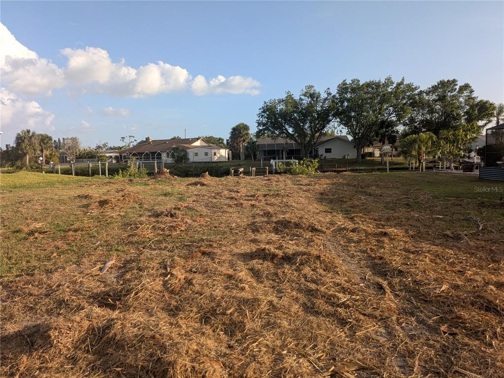 A vacant, grassy lot overlooks a canal with houses in the background — 18641 KLINGLER CIRCLE, PORT CHARLOTTE, FL