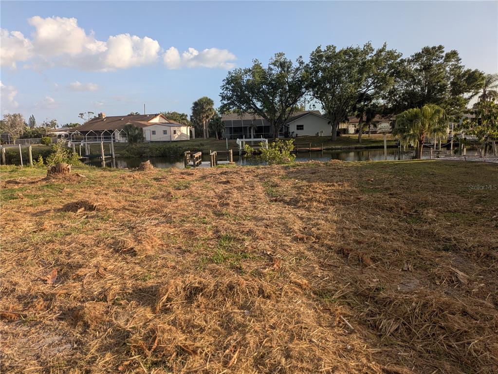 A vacant waterfront lot with dry grass and views of neighboring houses across a canal — 18641 KLINGLER CIRCLE, PORT CHARLOTTE, FL