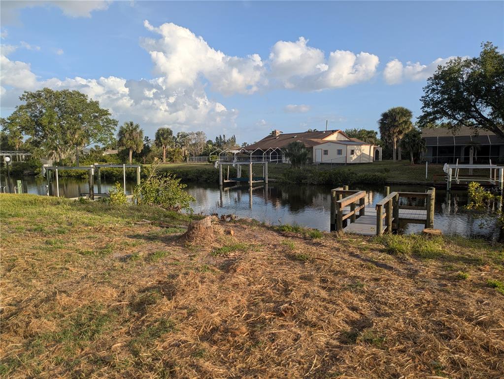 A canal view featuring a wooden dock, boat lifts, and a house in the background — 18641 KLINGLER CIRCLE, PORT CHARLOTTE, FL