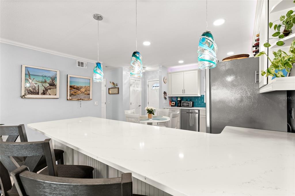 A kitchen features a white quartz island, pendant lights, and a dining area in the background — 1898 SHORE DRIVE S UNIT 319, SOUTH PASADENA, FL