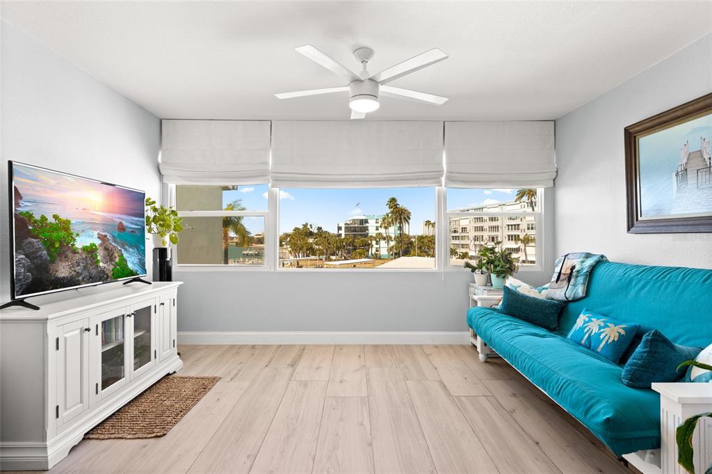 A living room features a bright blue sofa, a white media console, and large windows — 1898 SHORE DRIVE S UNIT 319, SOUTH PASADENA, FL