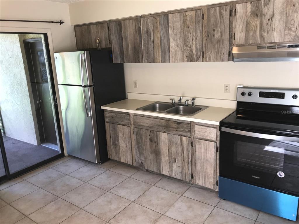 A kitchen features wood-look cabinets, a stainless steel refrigerator, a black stove, and tile flooring — 2806 46TH AVENUE DRIVE W, BRADENTON, FL