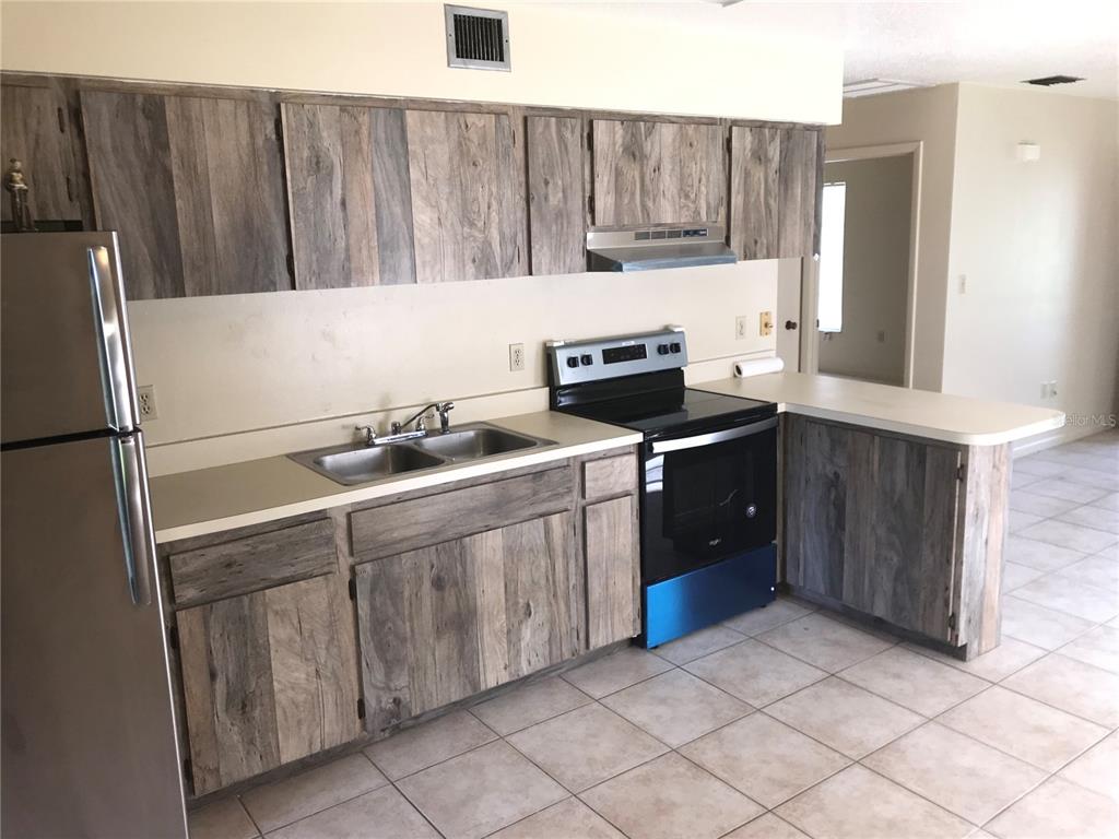 A kitchen features wood-look cabinets, stainless steel appliances, and light-colored tile flooring — 2806 46TH AVENUE DRIVE W, BRADENTON, FL