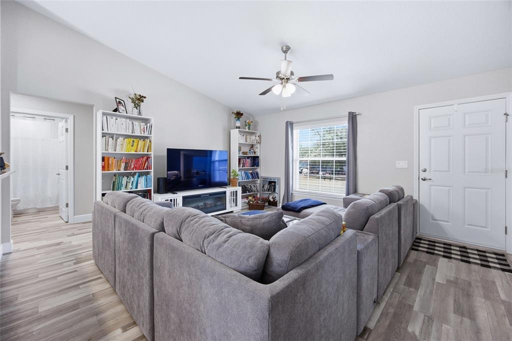 A living room features a large gray sectional sofa, bookshelves, a television, and wood-look flooring — 7728 SW 132ND PLACE, OCALA, FL