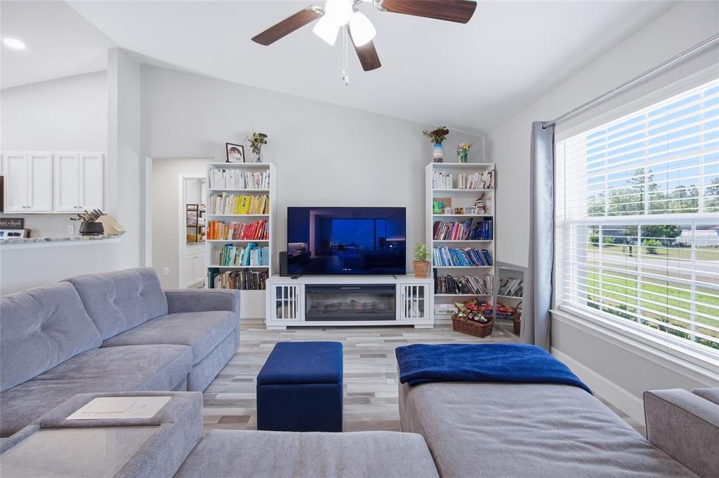 A living room features a grey sectional sofa, a television on a fireplace console, and bookshelves — 7728 SW 132ND PLACE, OCALA, FL