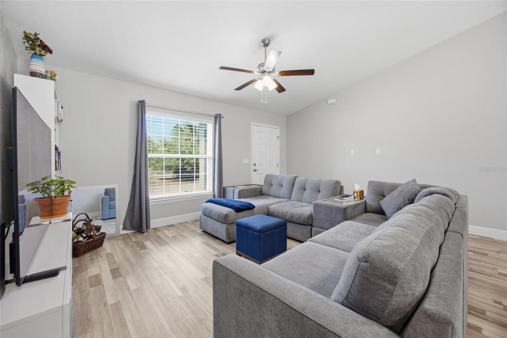 A living room features light wood-look flooring, a gray sectional sofa, and a ceiling fan — 7728 SW 132ND PLACE, OCALA, FL