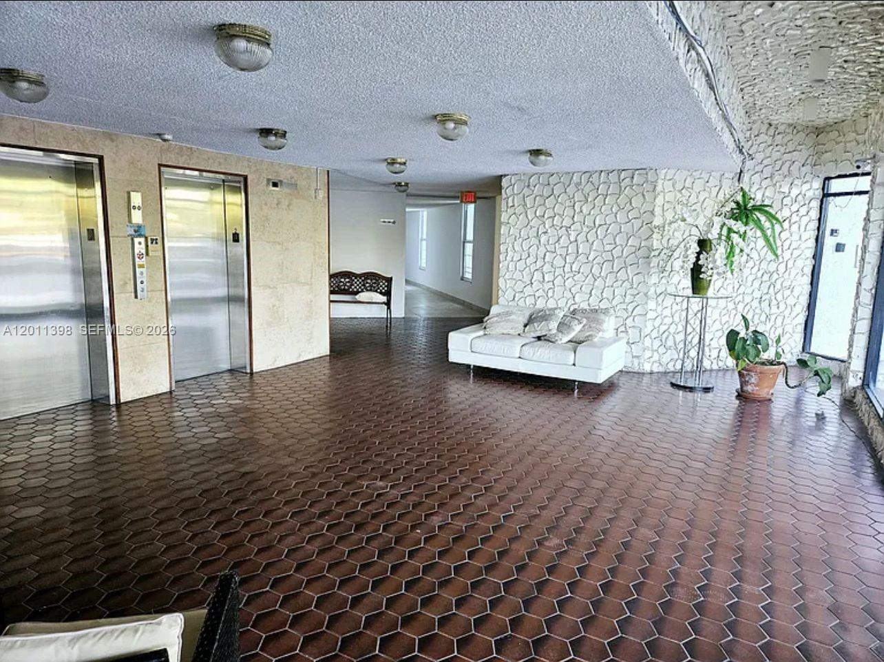 A lobby features a hexagonal tile floor, a white sofa, and a textured stone wall — 9682 Fontainebleau Blvd # 207, Miami FL 33172, MIAMI, FL
