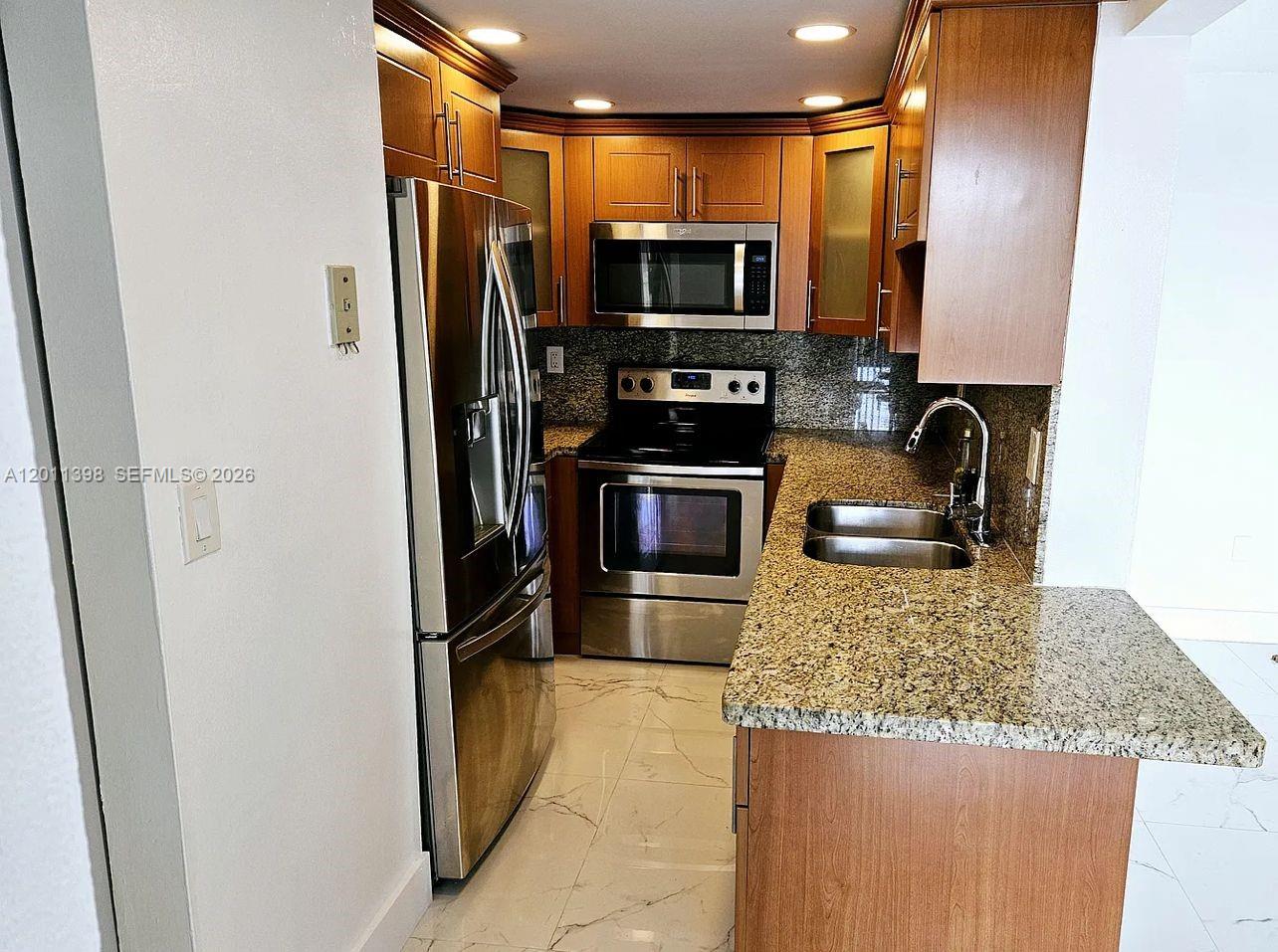 A kitchen features stainless steel appliances, wood cabinets, and granite countertops over tile flooring — 9682 Fontainebleau Blvd # 207, Miami FL 33172, MIAMI, FL