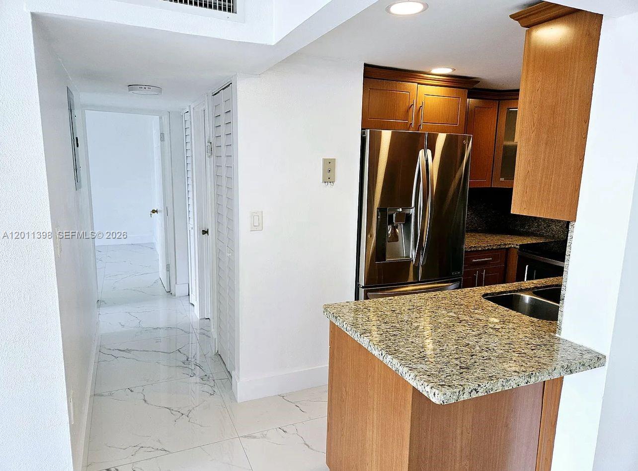 A kitchen with granite countertops and stainless steel appliances leads to a white-tiled hallway — 9682 Fontainebleau Blvd # 207, Miami FL 33172, MIAMI, FL