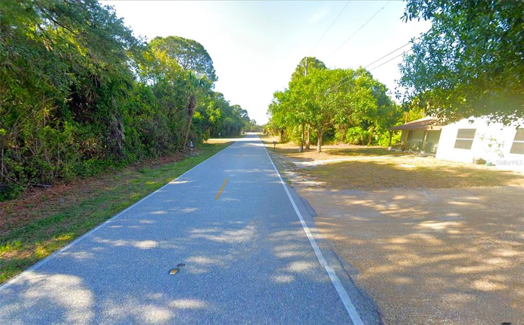 A paved road runs through a wooded area with a house visible on the right — 498 OVERBROOK STREET, PORT CHARLOTTE, FL