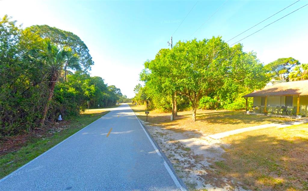 A paved road runs between a wooded area and a house with a front porch — 498 OVERBROOK STREET, PORT CHARLOTTE, FL