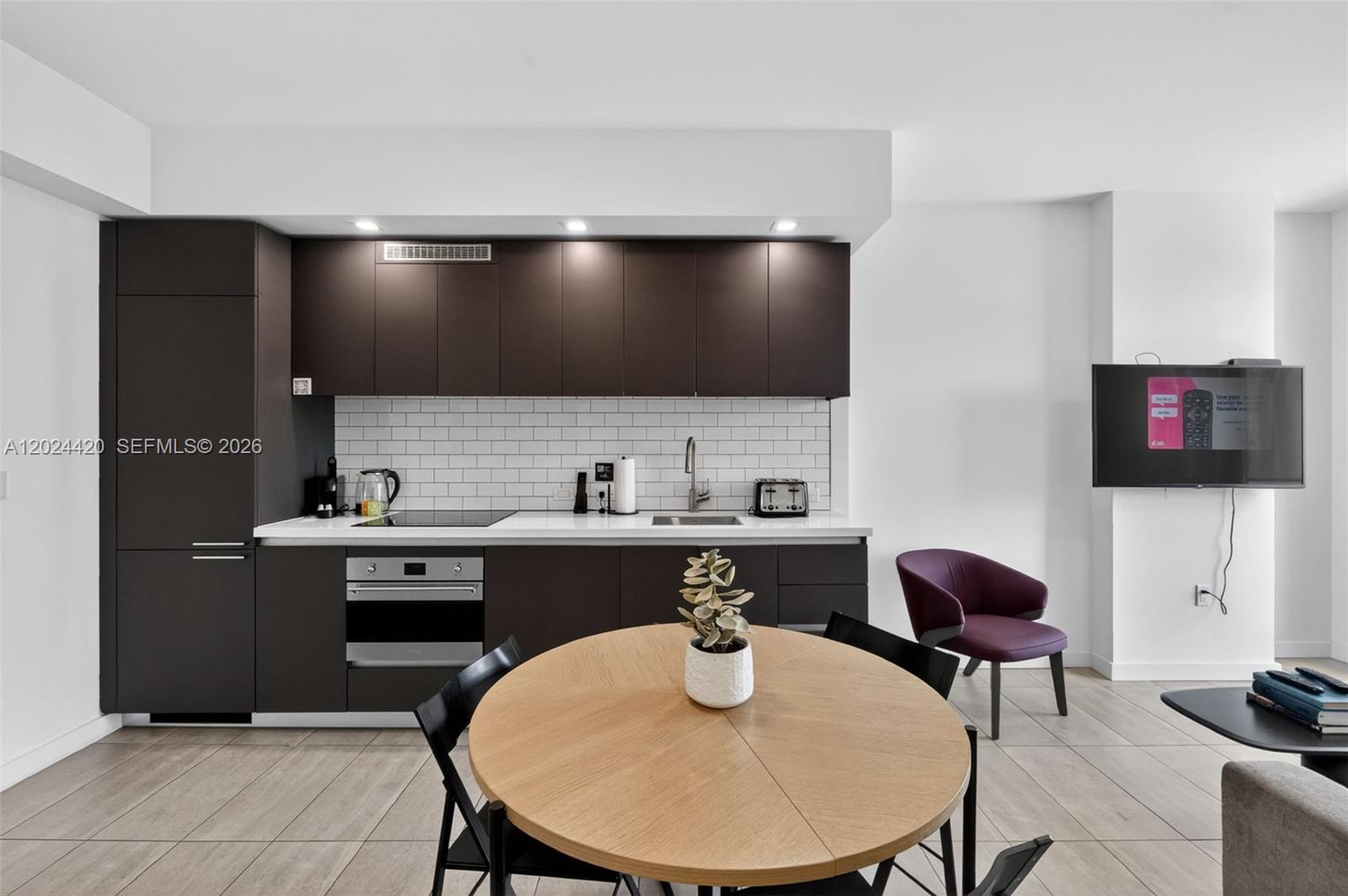 A modern kitchen features dark cabinetry, white subway tile backsplash, and an adjacent dining area — 227 NE 2nd St # 2805, Miami FL 33132, MIAMI, FL