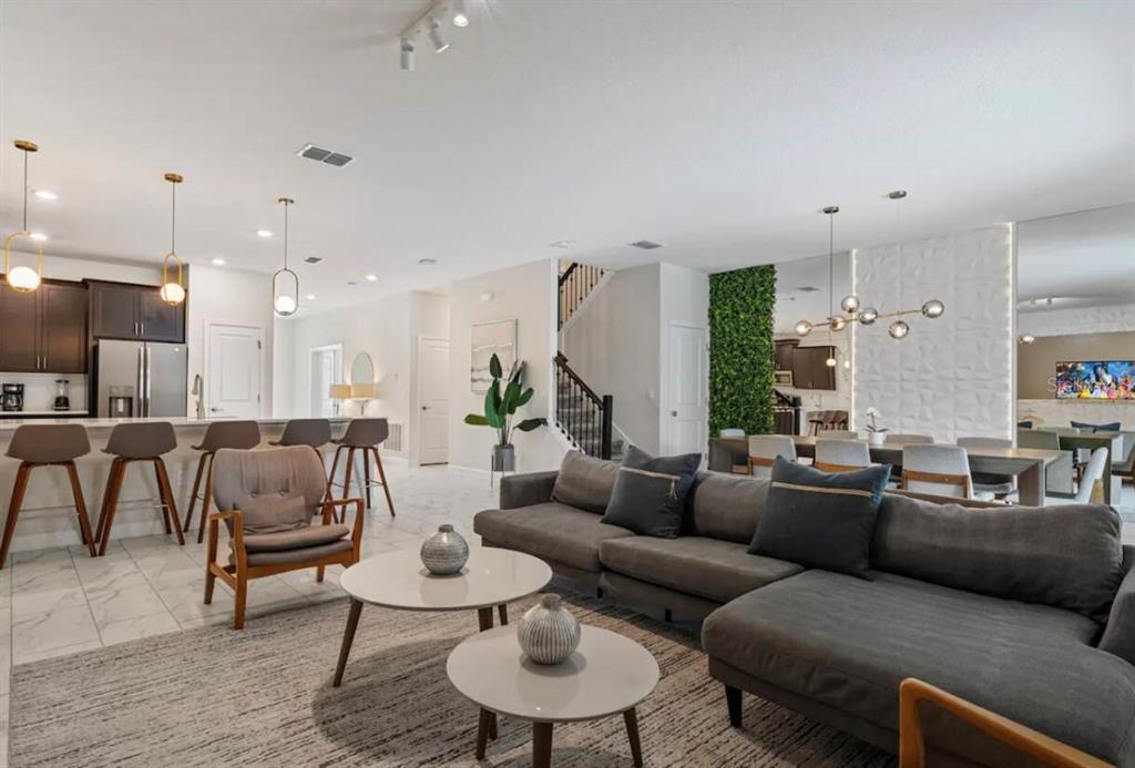 An open-concept living and dining area features a gray sectional, kitchen island, and staircase — 4525 TARGET BOULEVARD, KISSIMMEE, FL