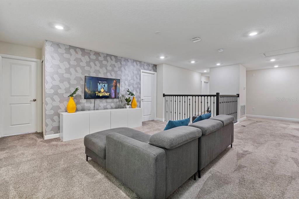A carpeted loft features a gray sectional sofa, a television on a white console, and patterned wallpaper — 4525 TARGET BOULEVARD, KISSIMMEE, FL