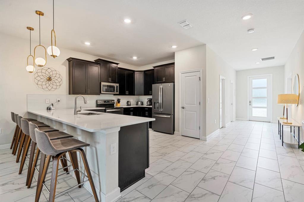 A modern kitchen features dark cabinetry, white countertops, a breakfast bar, and tiled flooring — 4525 TARGET BOULEVARD, KISSIMMEE, FL