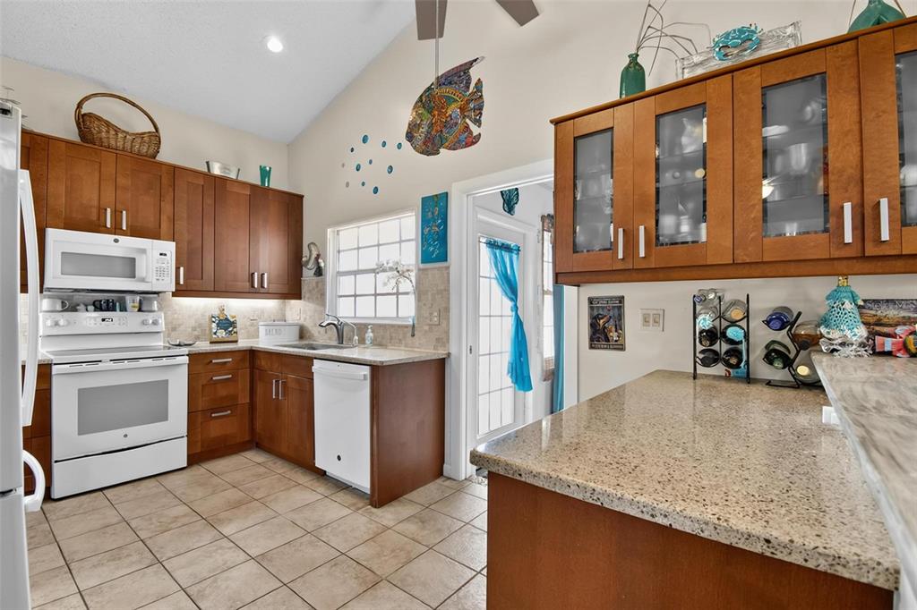 A kitchen features wood cabinets, granite countertops, white appliances, and tile flooring under a vaulted ceiling — 15 SEA VISTA DRIVE, PALM COAST, FL