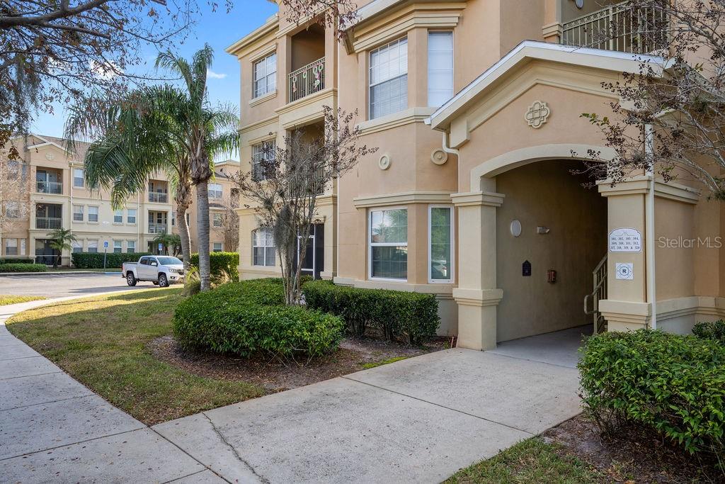 A multi-story apartment building exterior features tan stucco walls, a covered entryway, and landscaping — 302 TERRACE RIDGE CIRCLE UNIT 302, DAVENPORT, FL
