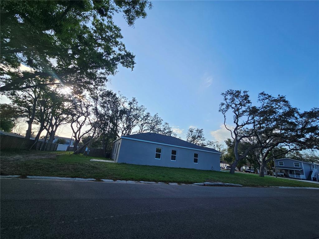 A gray, single-story house sits on a grassy lot surrounded by large trees — 4502 42ND AVENUE N, ST PETERSBURG, FL