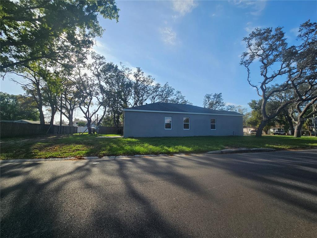 A gray, single-story house sits on a grassy lot next to large trees — 4502 42ND AVENUE N, ST PETERSBURG, FL