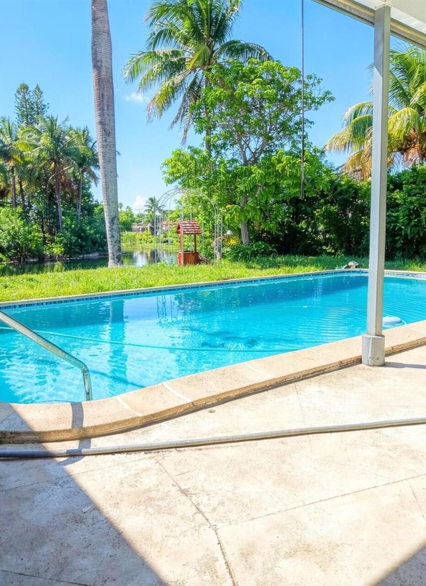 A swimming pool sits on a patio overlooking a grassy yard with a wishing well — 6641 Miramar Parkway, Miramar FL 33023, MIRAMAR, FL