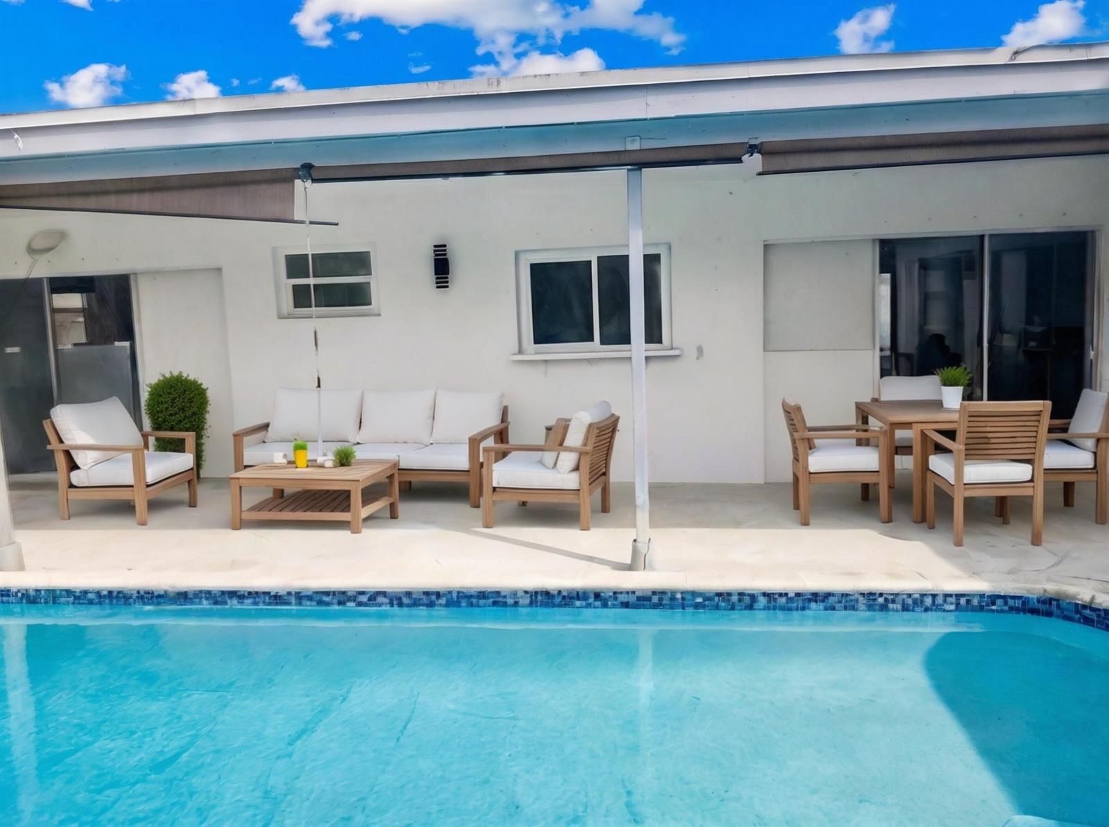 A patio with wooden furniture and white cushions overlooks a swimming pool — 6641 Miramar Parkway, Miramar FL 33023, MIRAMAR, FL