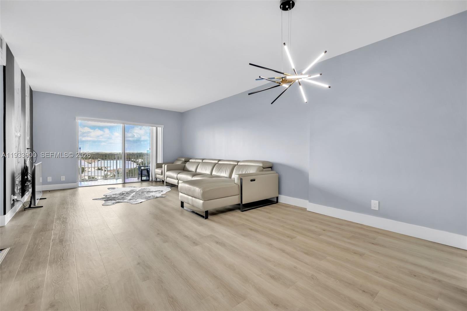 A living room features light wood flooring, a beige sectional sofa, and a modern chandelier — 4200 Hillcrest Dr # 802, Hollywood FL 33021, HOLLYWOOD, FL