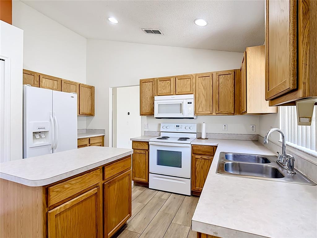 A kitchen features oak cabinets, white appliances, laminate countertops, and wood-look tile flooring — 1029 BRAYTON LANE, DAVENPORT, FL