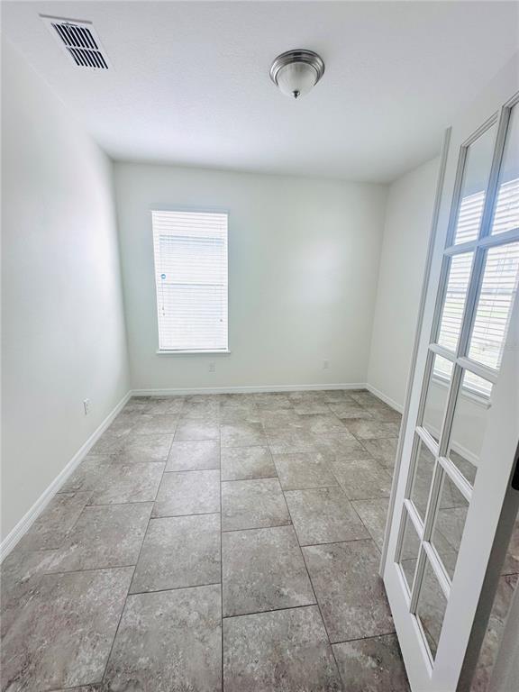 An empty room with light-colored walls, tile flooring, a window with blinds, and French doors — 16488 CENTIPEDE STREET, CLERMONT, FL