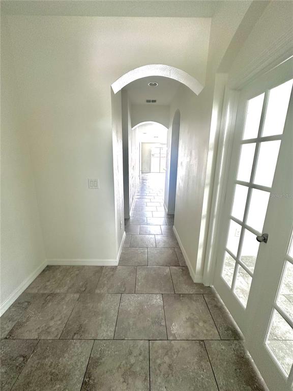 A tiled hallway features arched entryways and a white French door on the right — 16488 CENTIPEDE STREET, CLERMONT, FL