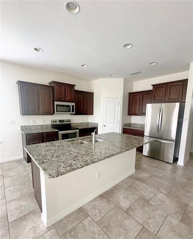 A kitchen features dark wood cabinets, granite countertops, a center island, and stainless steel appliances — 16488 CENTIPEDE STREET, CLERMONT, FL