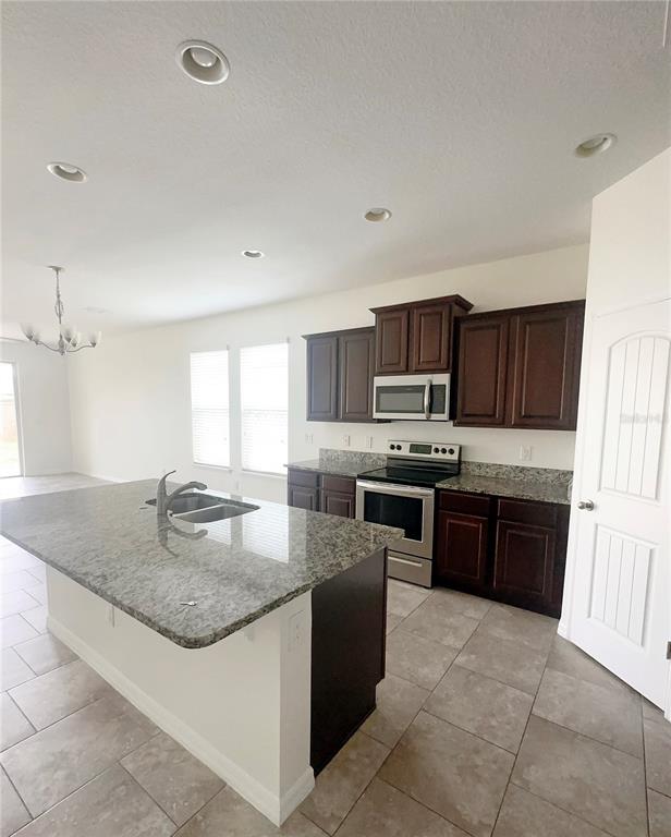 A kitchen features dark wood cabinets, granite countertops, a center island, and tile flooring — 16488 CENTIPEDE STREET, CLERMONT, FL