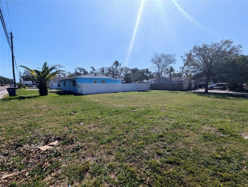 A vacant grassy lot sits in front of a blue house with a white fence — 3990 54TH AVENUE N, ST PETERSBURG, FL