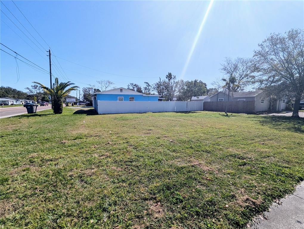 A vacant, grassy lot sits in front of a blue house with a white fence — 3990 54TH AVENUE N, ST PETERSBURG, FL