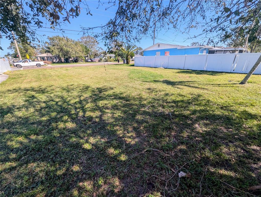 A vacant grassy lot features a white vinyl fence and a blue house in the background — 3990 54TH AVENUE N, ST PETERSBURG, FL