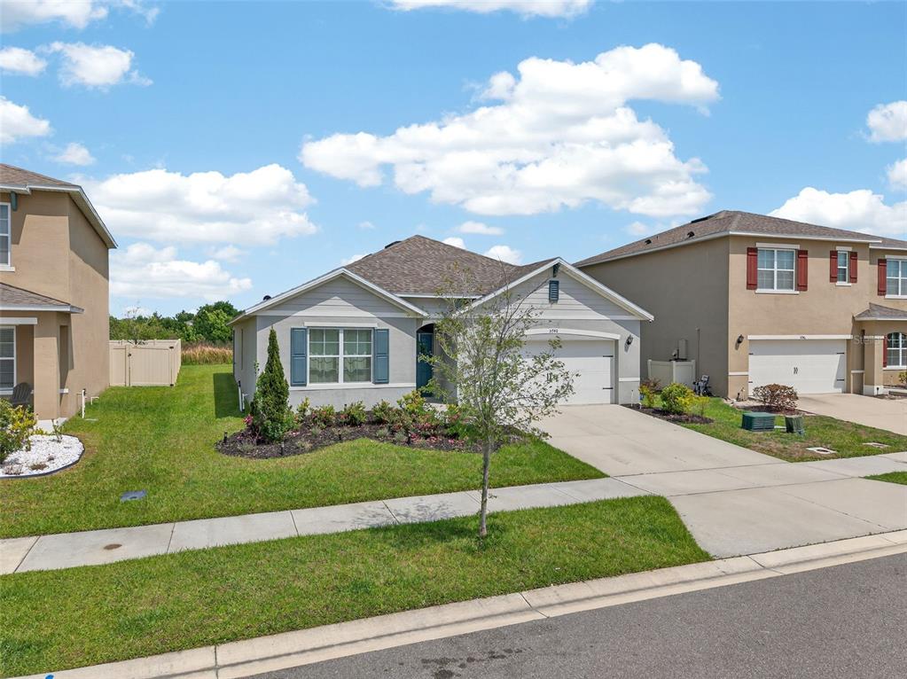 A single-story house with a light-colored exterior, a two-car garage, and a landscaped front yard — 5740 GREY GRANITE WAY, LAKELAND, FL
