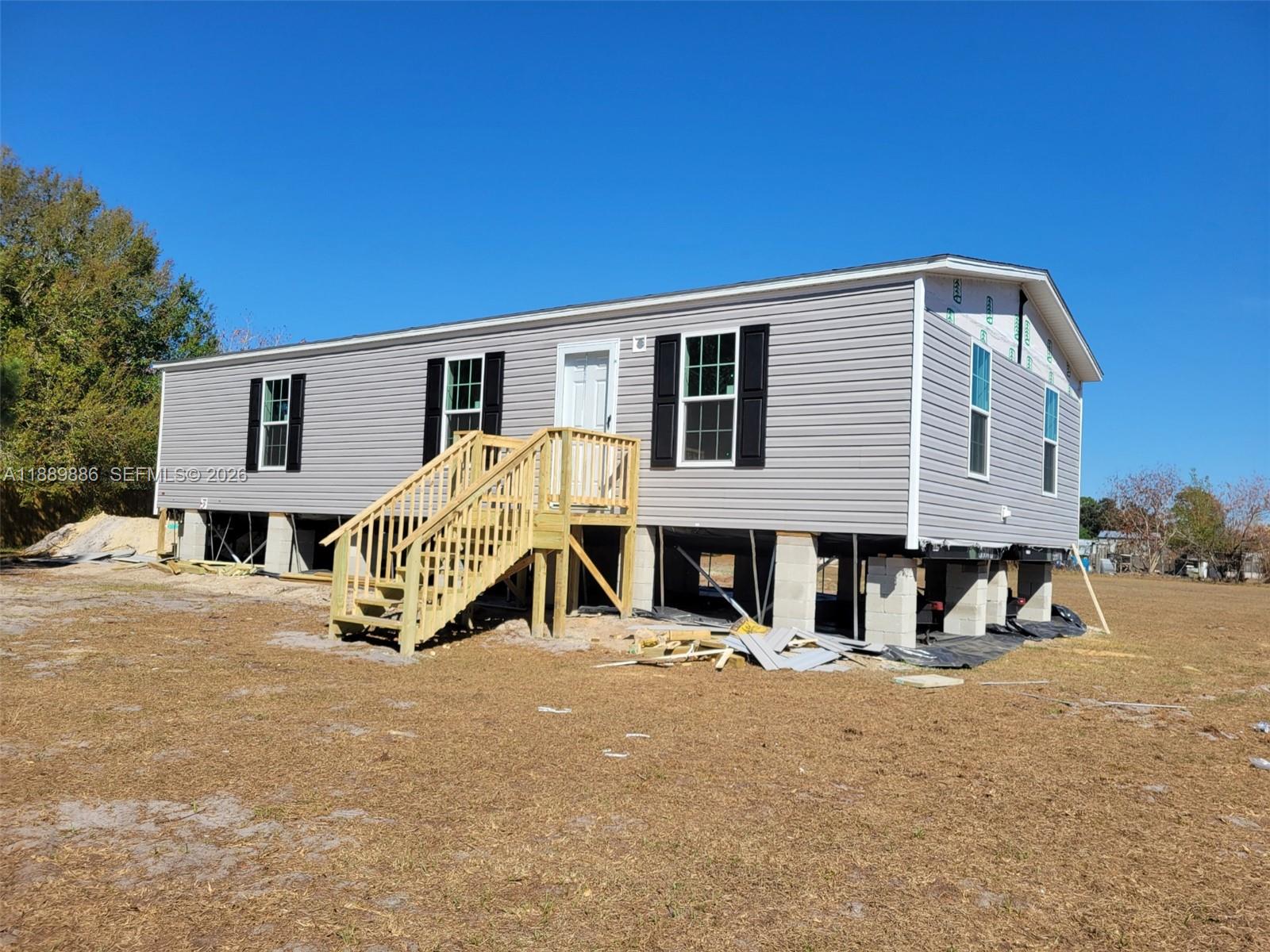 A light gray manufactured home sits on concrete block piers with wooden stairs leading up — 357 Horse Club, Clewiston FL 33440, CLEWISTON, FL